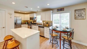 A modern kitchen with white cabinetry, stainless steel appliances, and a central island with stools. - Lakeview Lodge - Stay for 6 (Lake Geneva)
