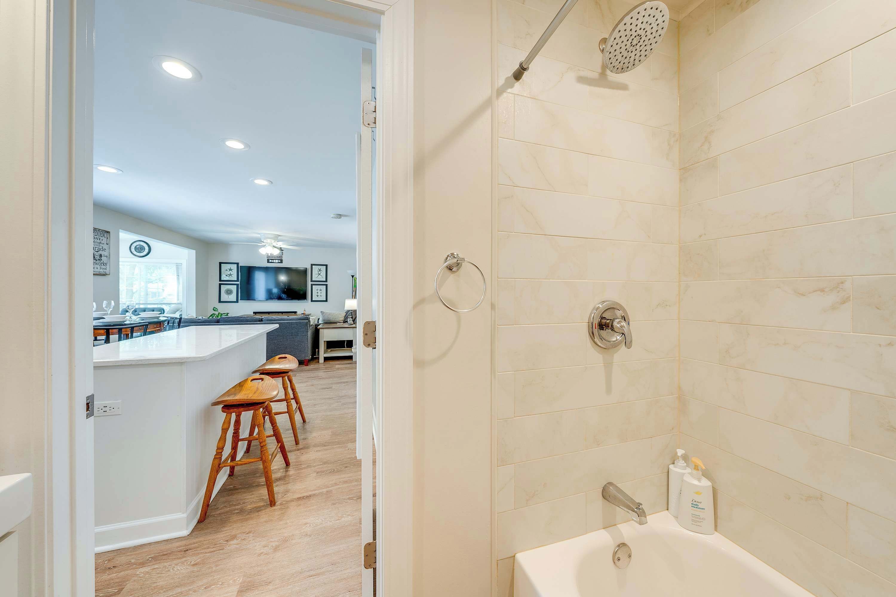 A modern bathroom with a bathtub, shower, and toilet. There is a bar area with stools visible in the background.