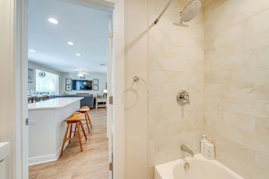 A modern bathroom with a bathtub, shower, and toilet. There is a bar area with stools visible in the background. - Lakeview Lodge - Stay for 6 (Lake Geneva)