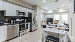 A modern kitchen with stainless steel appliances, a dining area with a table set for four, and a living area with a sofa and TV. - Modern large 2-bedroom near Philadelphia Convention Center!!! (Philadelphia)
