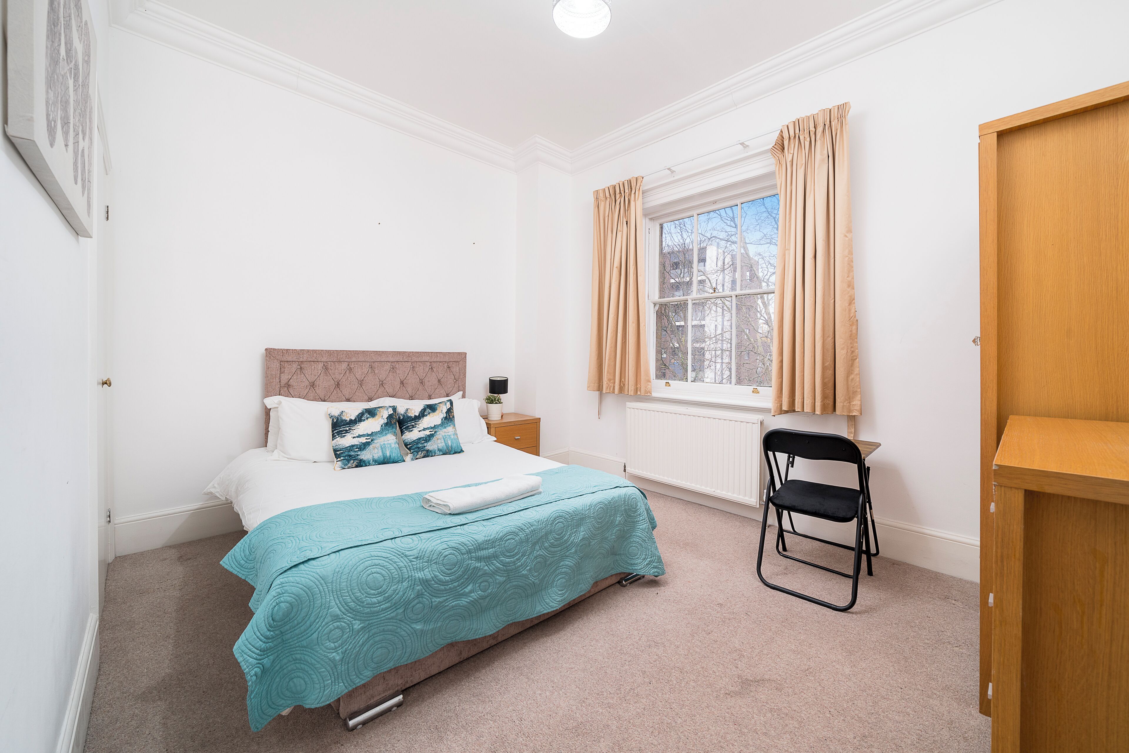 A neatly arranged bedroom with a bed, a chair, a nightstand, and a window with curtains.