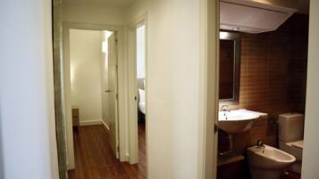 A narrow hallway leading to a bathroom with a sink, bidet, and a mirror.