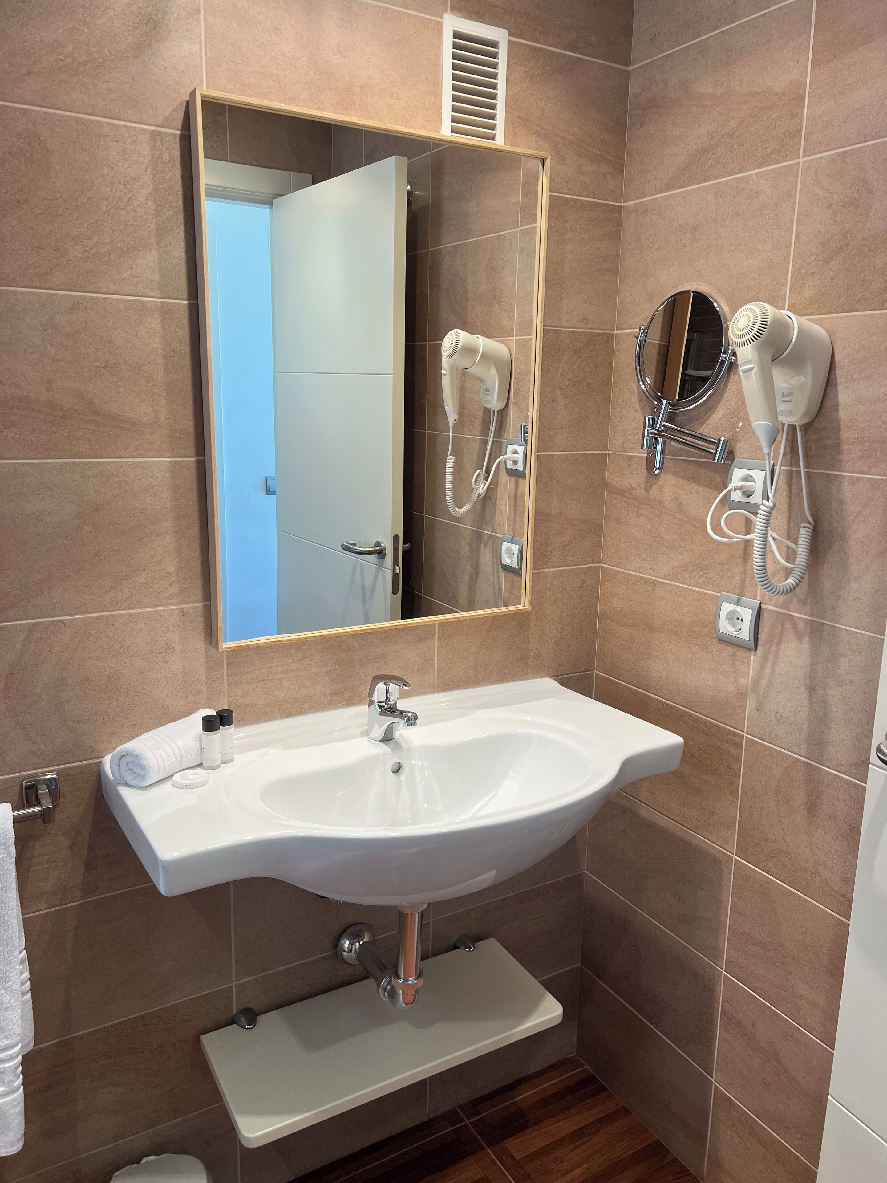 Een badkamer met een witte wastafel, een spiegel en twee haardrogerhouders aan de muur.