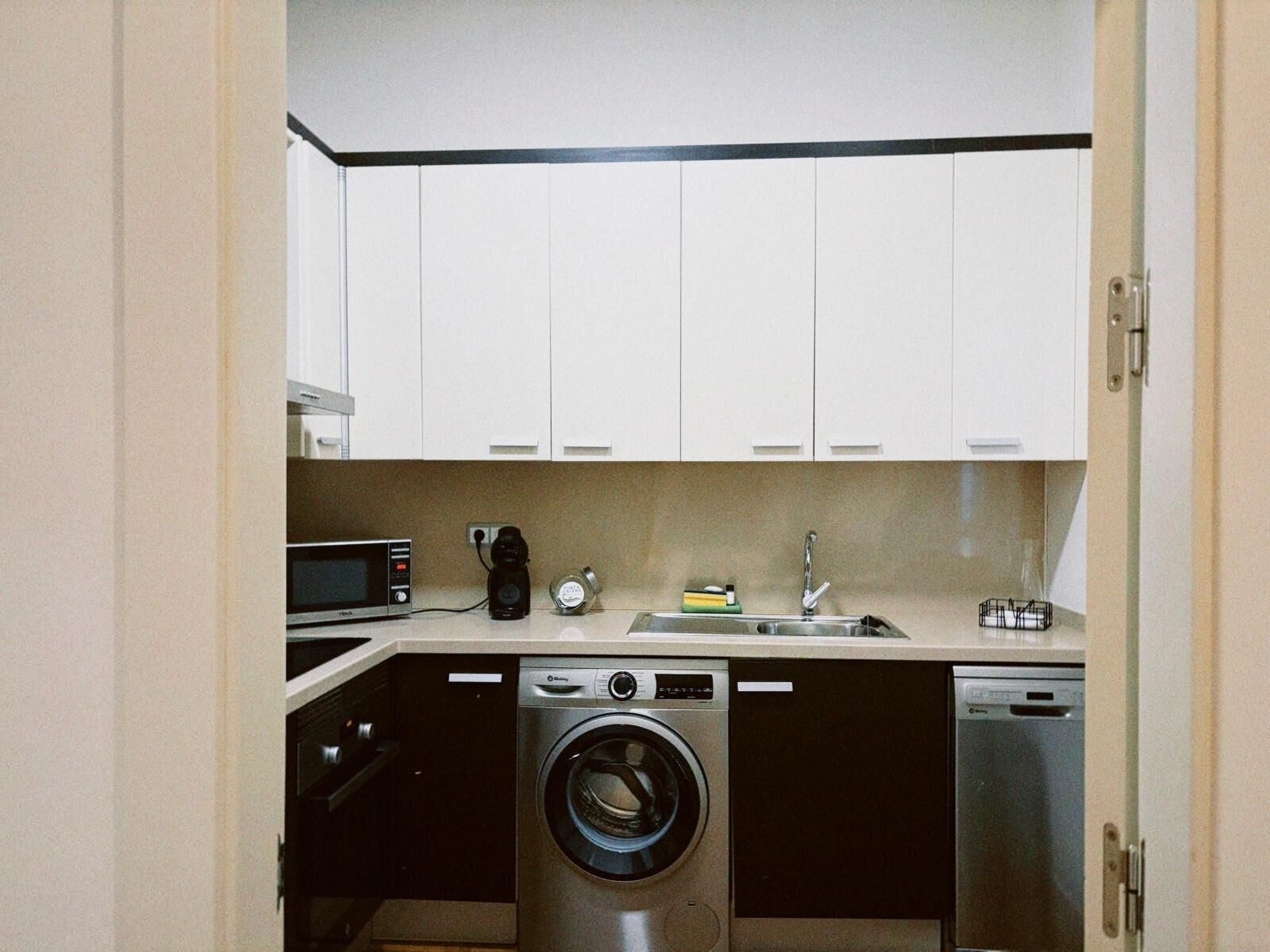 A compact kitchen with a washing machine, dishwasher, microwave, and a coffee maker.