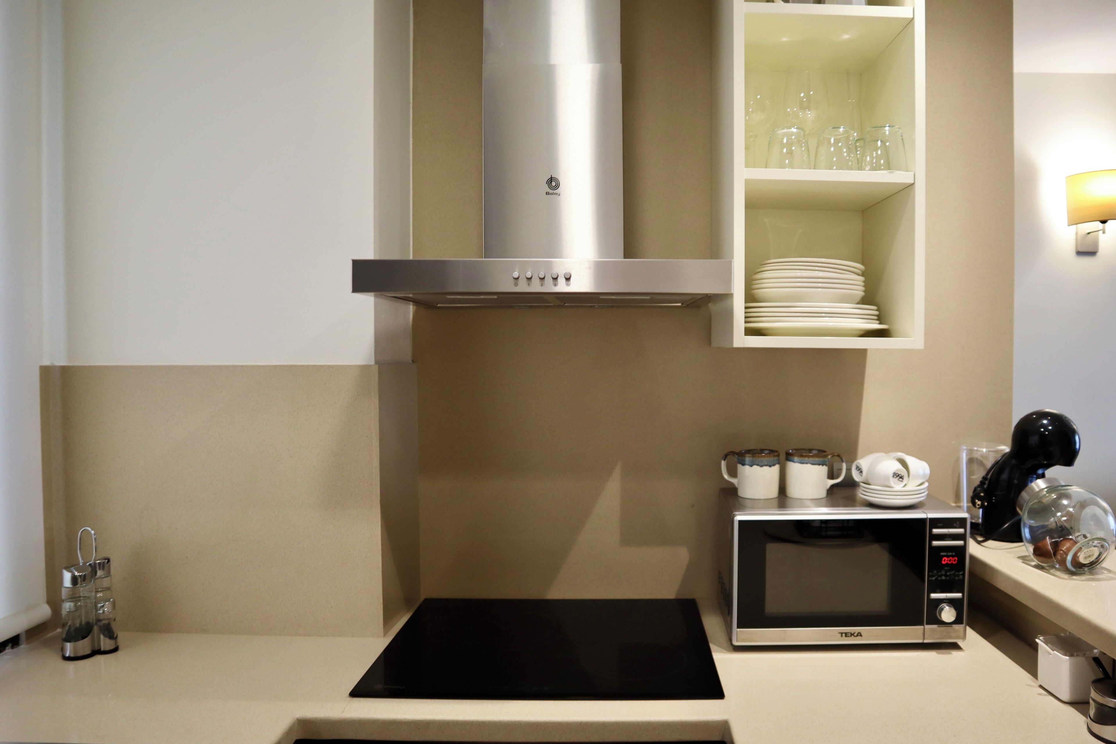 A kitchen with a microwave, a stove, and a cabinet above it containing glassware and plates.