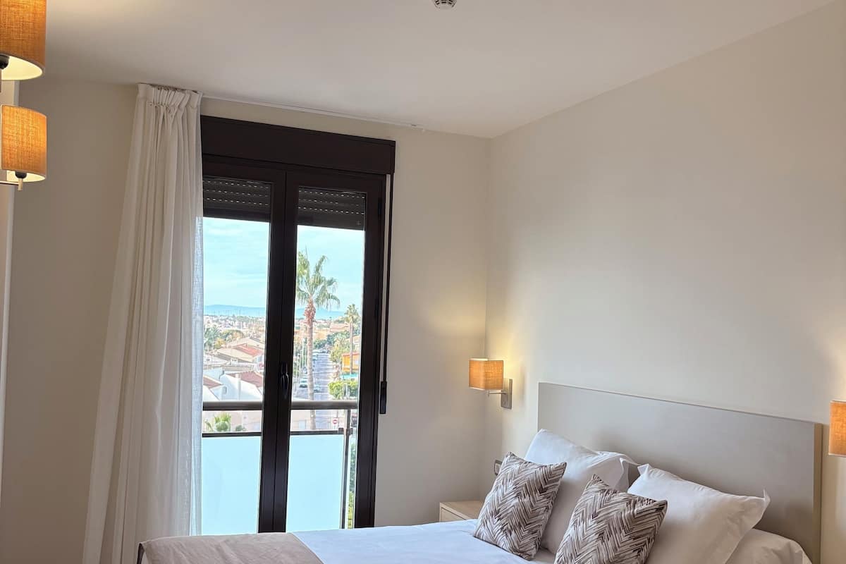 A hotel room with a large bed, a view of the city through the window, and a balcony.