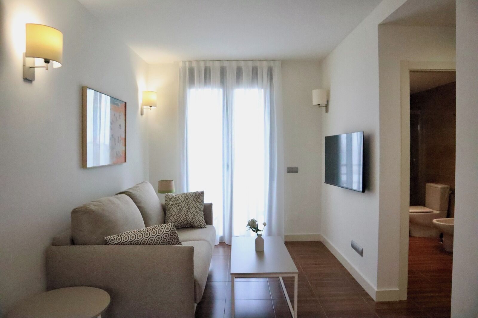 Een moderne woonkamer met een bank, salontafel en een aan de muur bevestigde televisie.
