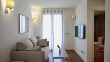 Een moderne woonkamer met een bank, salontafel en een aan de muur bevestigde televisie.