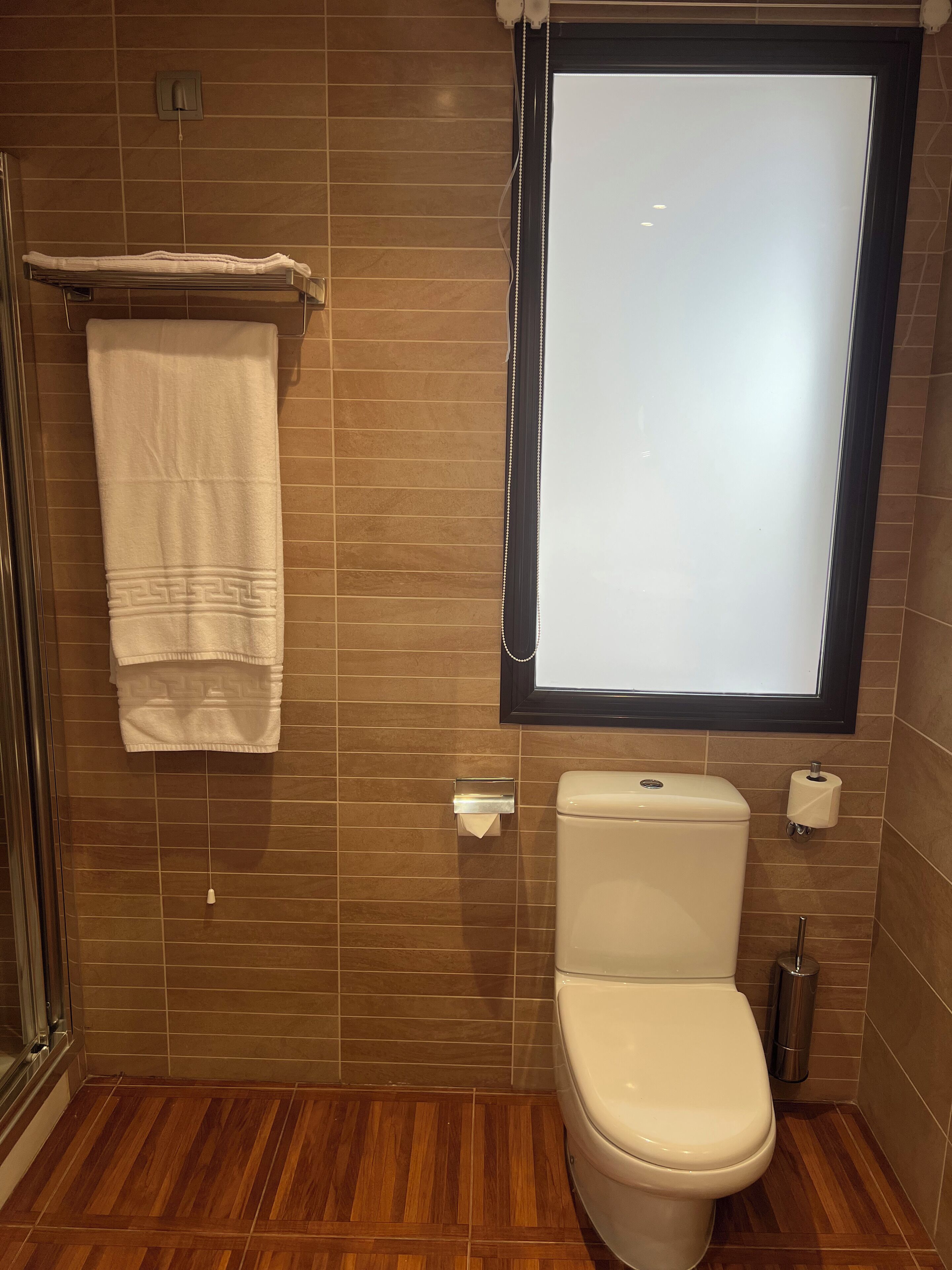 Une salle de bain équipée de toilettes, d’un porte-serviettes, d’une fenêtre et d’une poubelle.