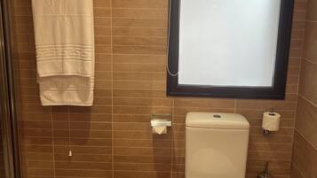 Une salle de bain équipée de toilettes, d’un porte-serviettes, d’une fenêtre et d’une poubelle.