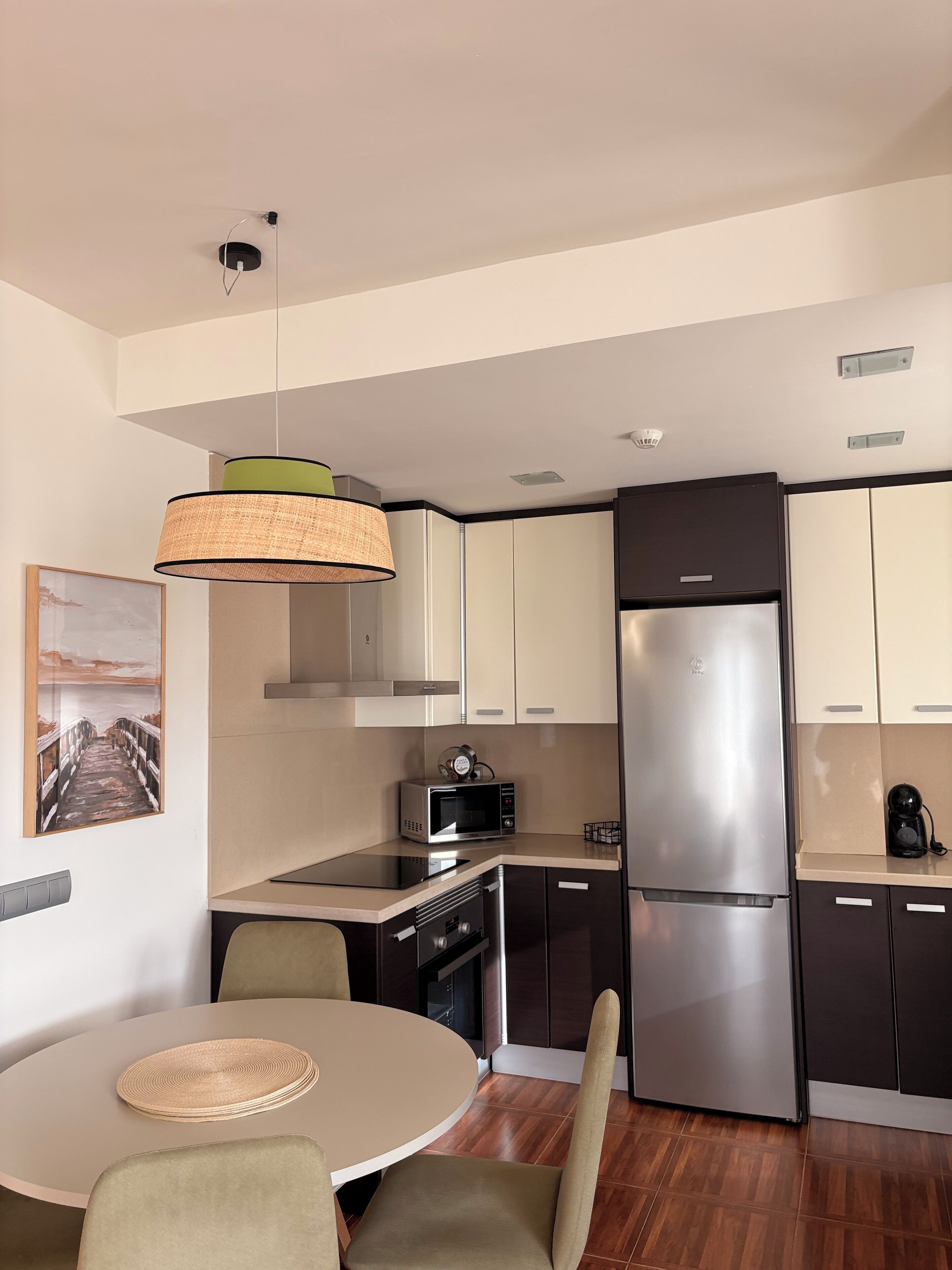 Una cocina moderna con una mesa de comedor redonda, sillas, una lámpara colgante y electrodomésticos de acero inoxidable.