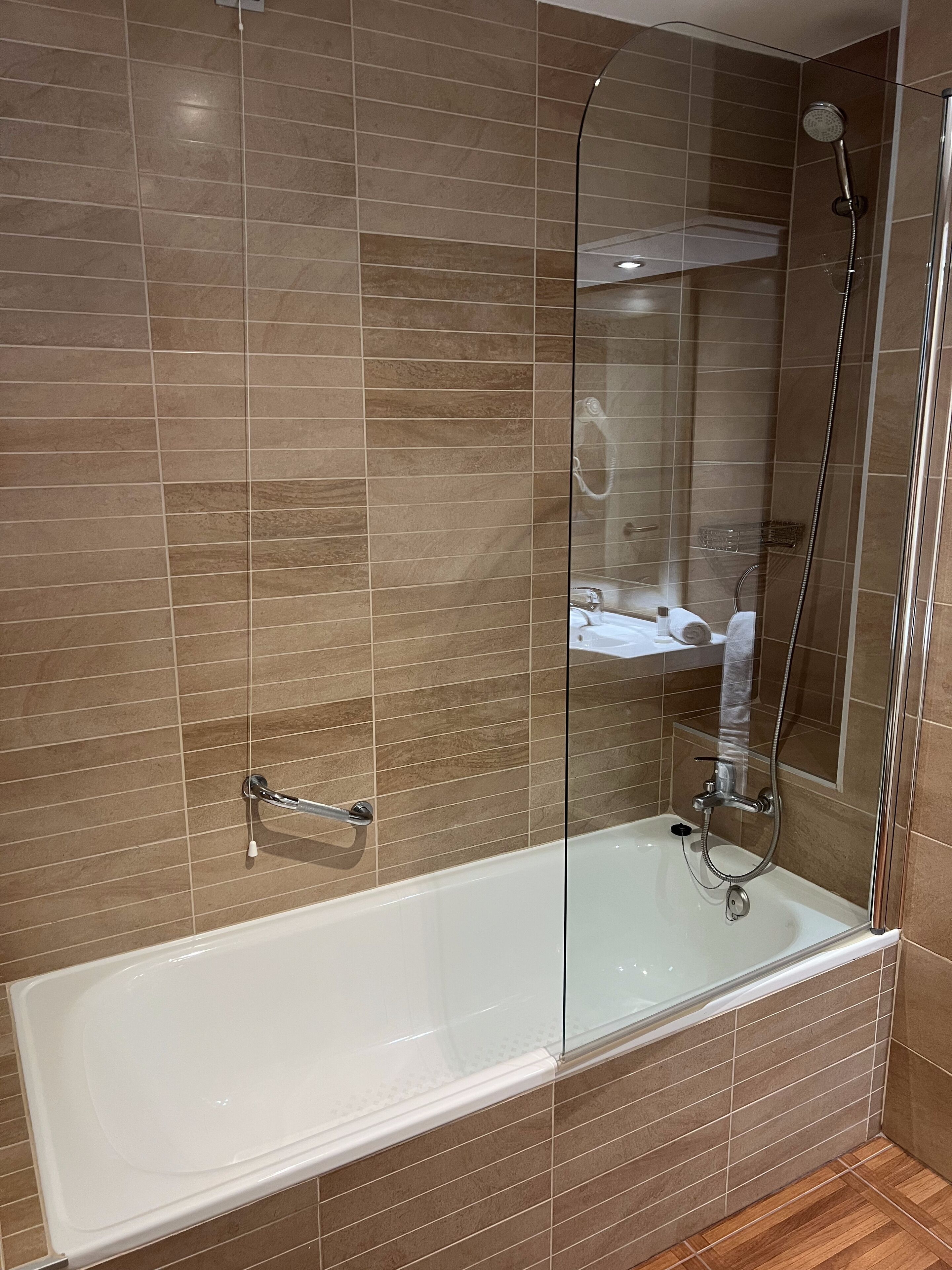 Un baño moderno con ducha de vidrio, bañera blanca y zona de lavamanos visible.