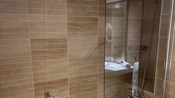 Un baño moderno con ducha de vidrio, bañera blanca y zona de lavamanos visible.
