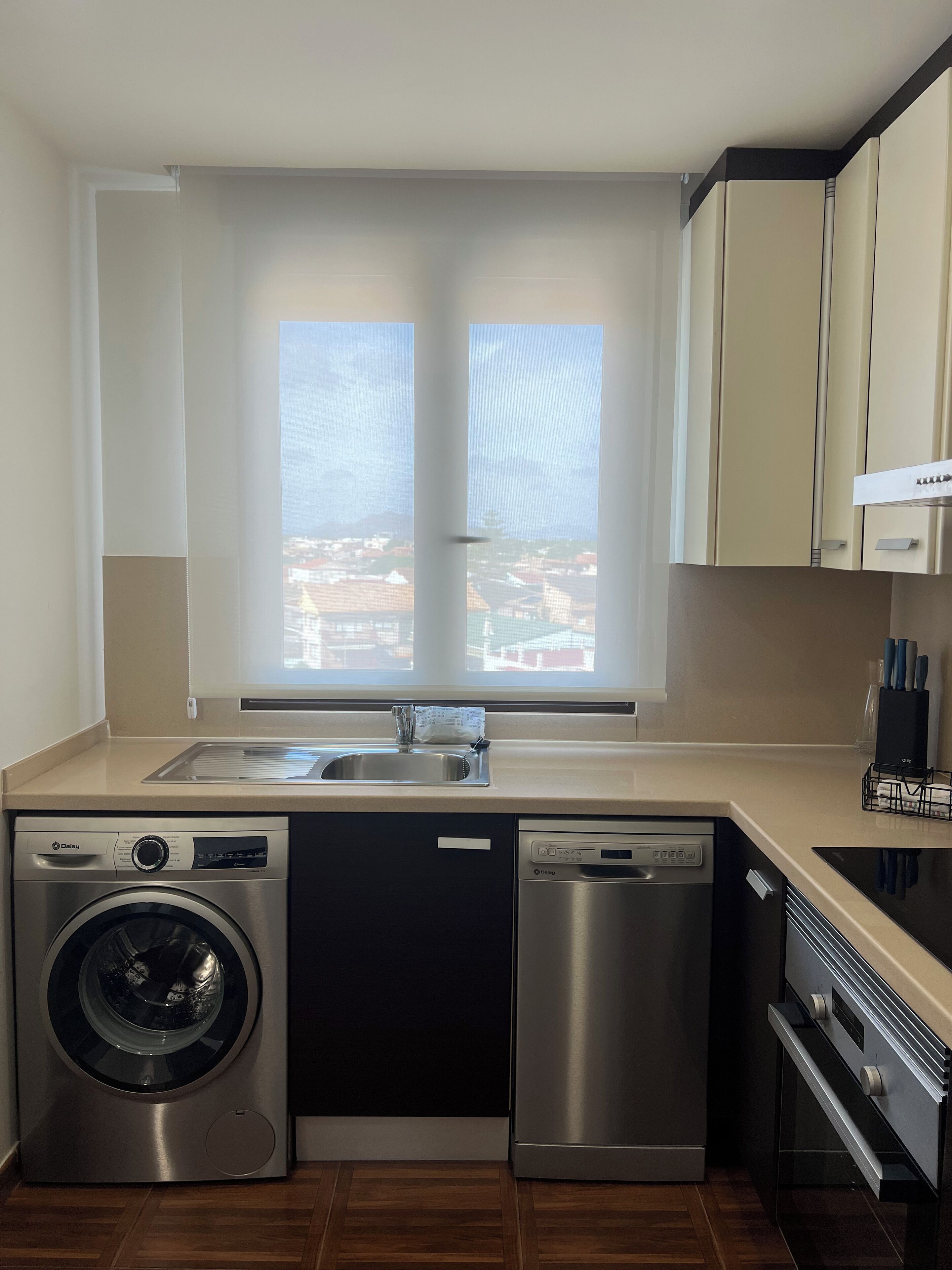 A compact kitchen with a washing machine, dishwasher, and oven. It features a window with a view of buildings outside.