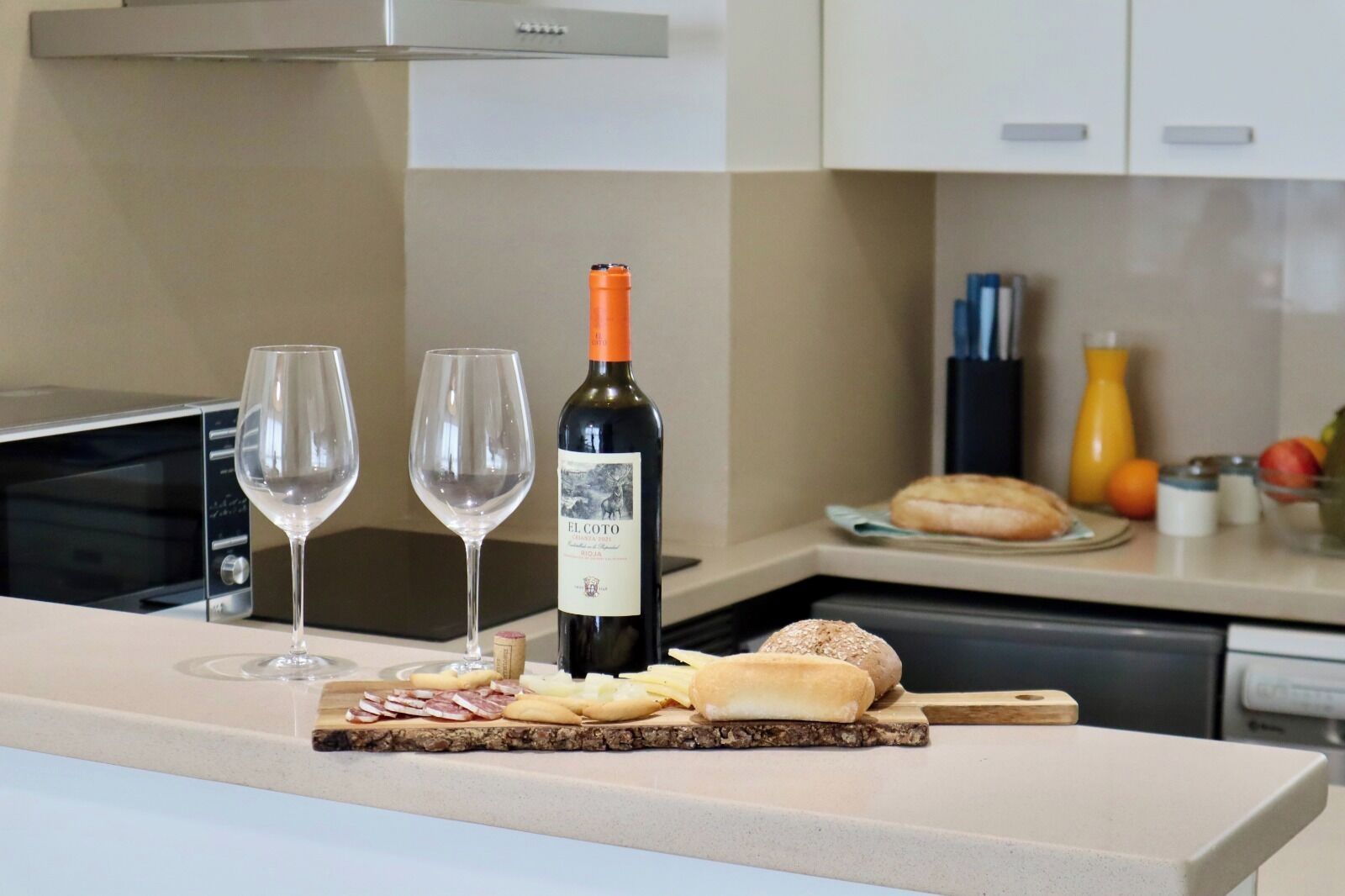 Eine Küchenarbeitsplatte mit einer Flasche El Coto Wein, zwei Gläsern und verschiedenen Snacks.