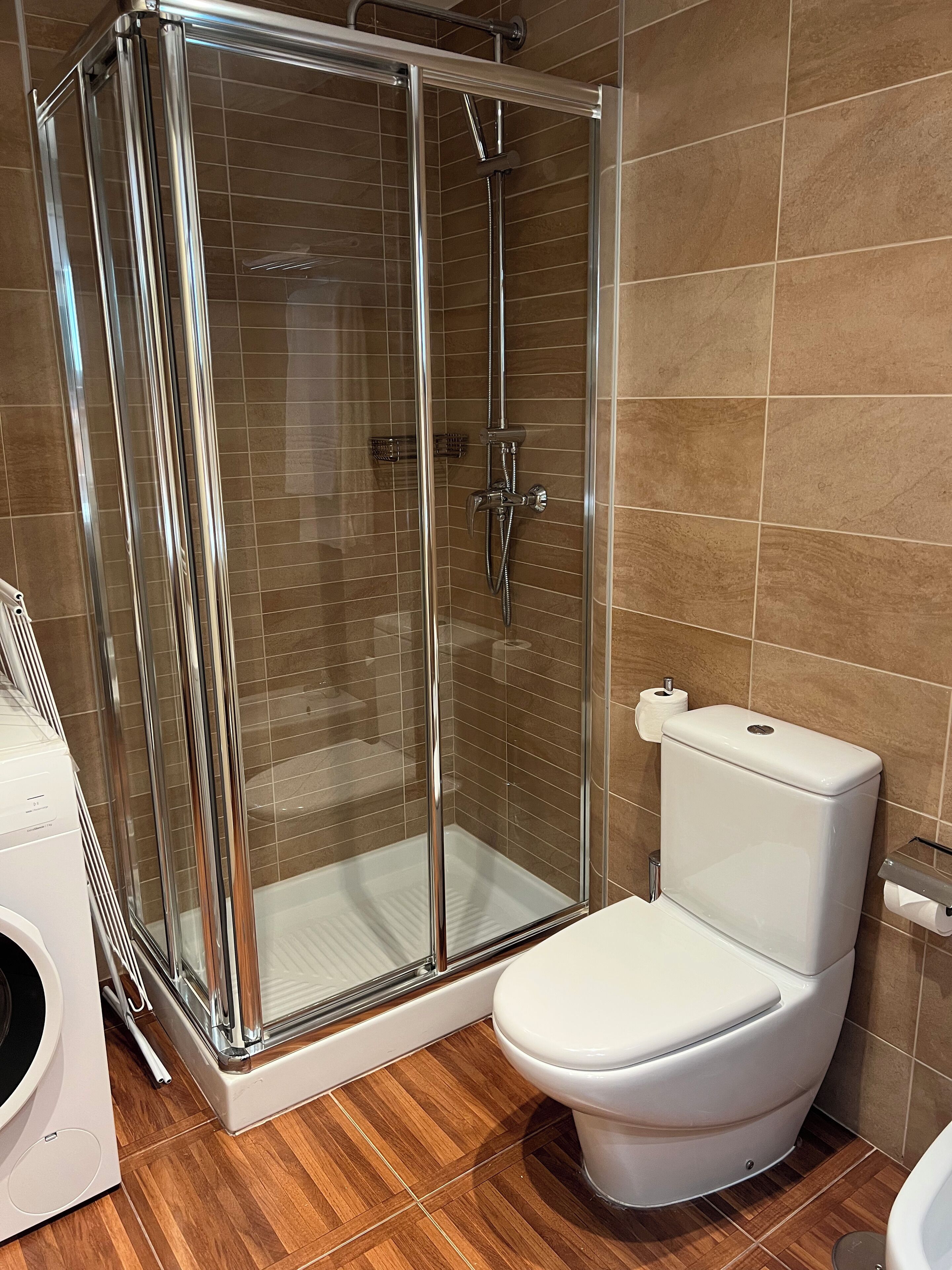 A bathroom with a glass-enclosed shower, a white toilet, and a washing machine.