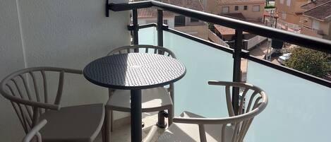 A balcony with a table and chairs, overlooking a coastal view with palm trees and buildings.