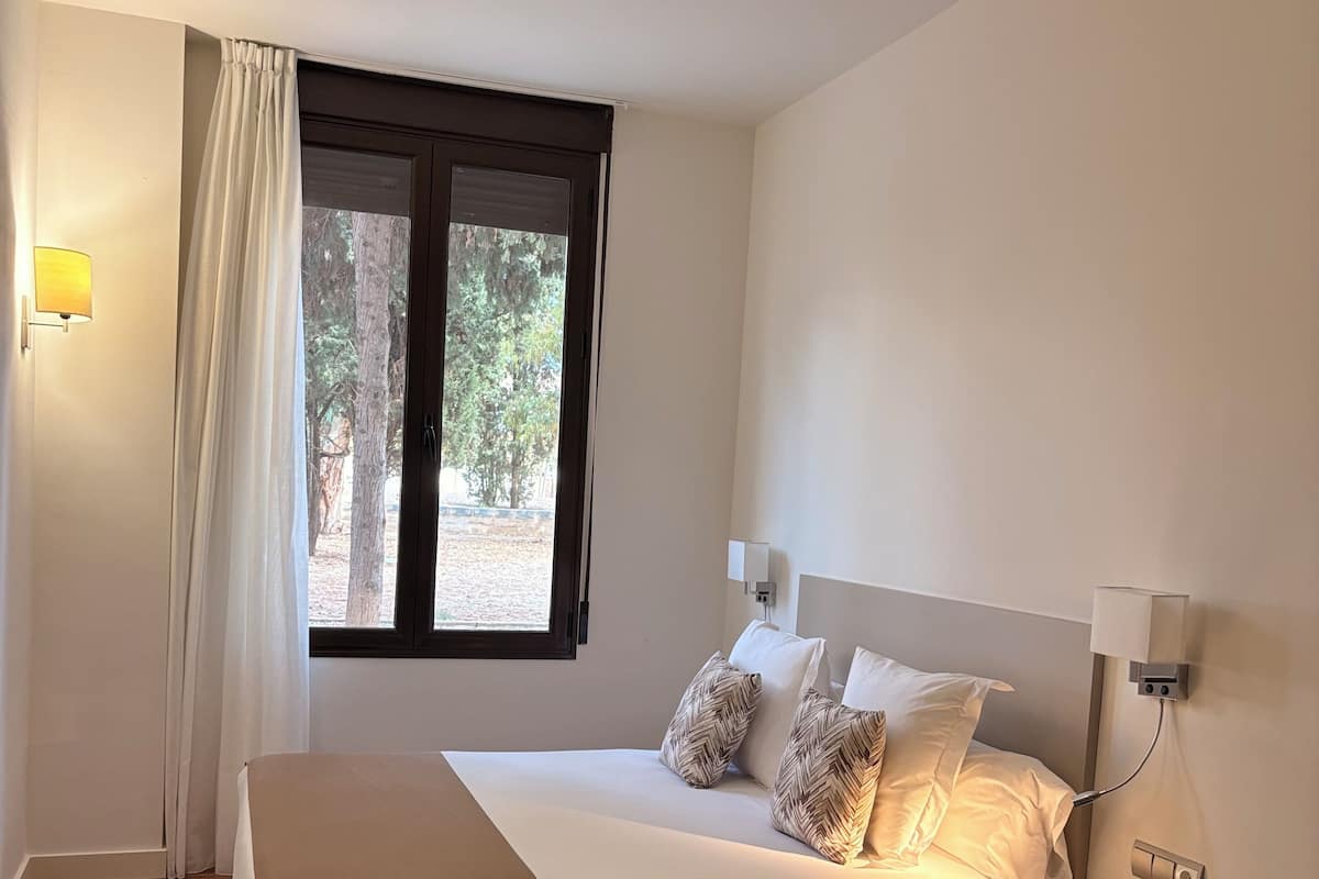 A neatly arranged bedroom with a bed, bedside table, lamp, and a window with curtains.