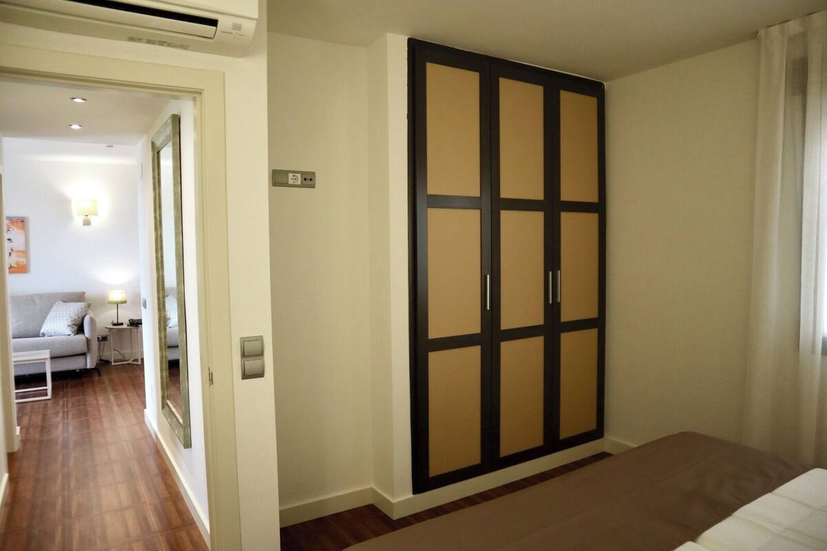 A bedroom with a bed, a wardrobe, and a small sitting area with a sofa and a table.