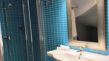 Un baño con ducha de mampara de vidrio, lavamanos blanco y espejo con marco dorado.