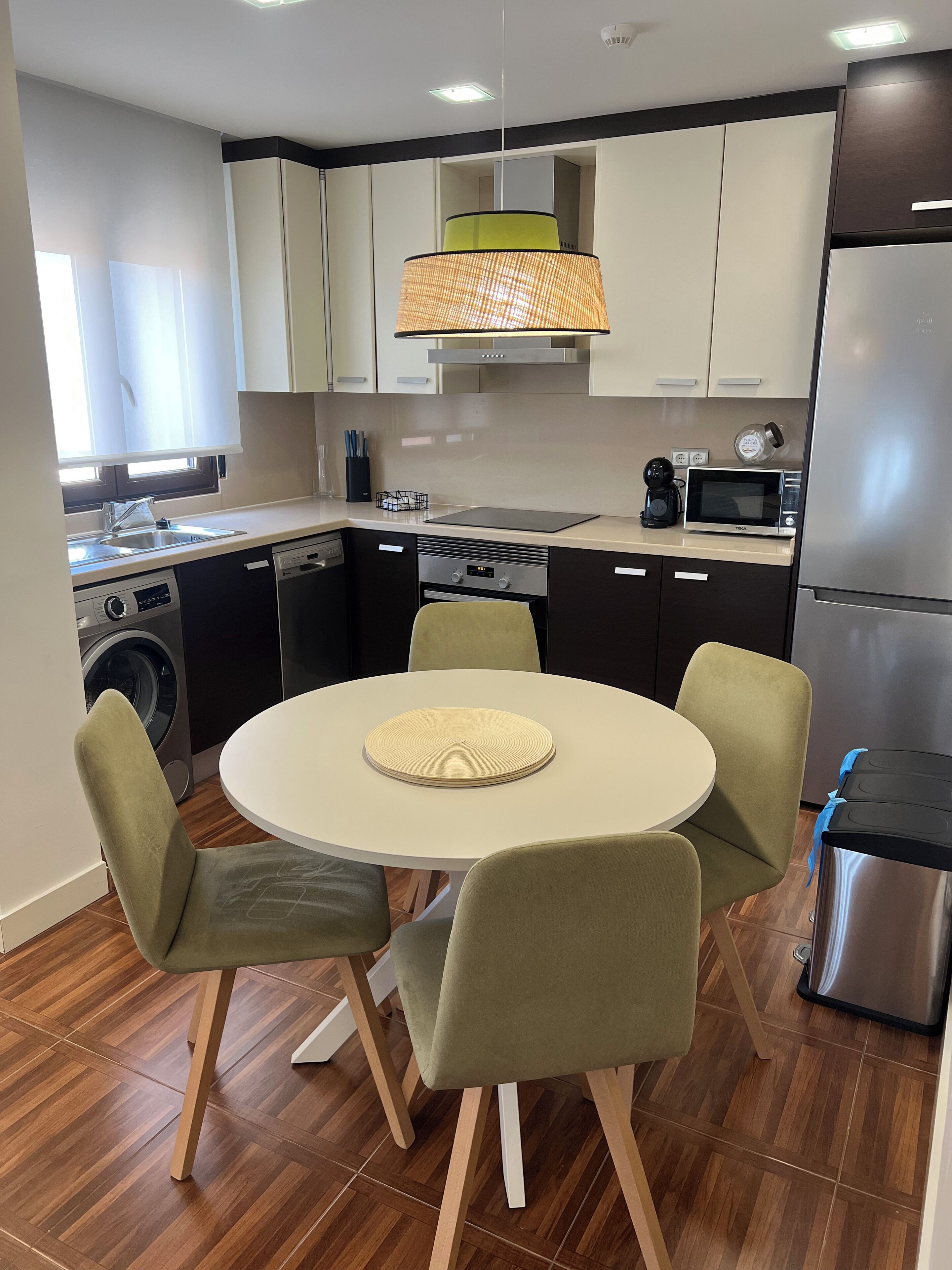 Una cocina moderna con una mesa redonda, sillas, un microondas y un refrigerador.