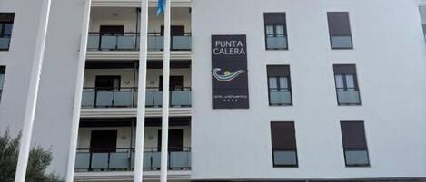 A multi-story building with balconies, a sign reading "PUNTA CALERA," and flags on flagpoles.