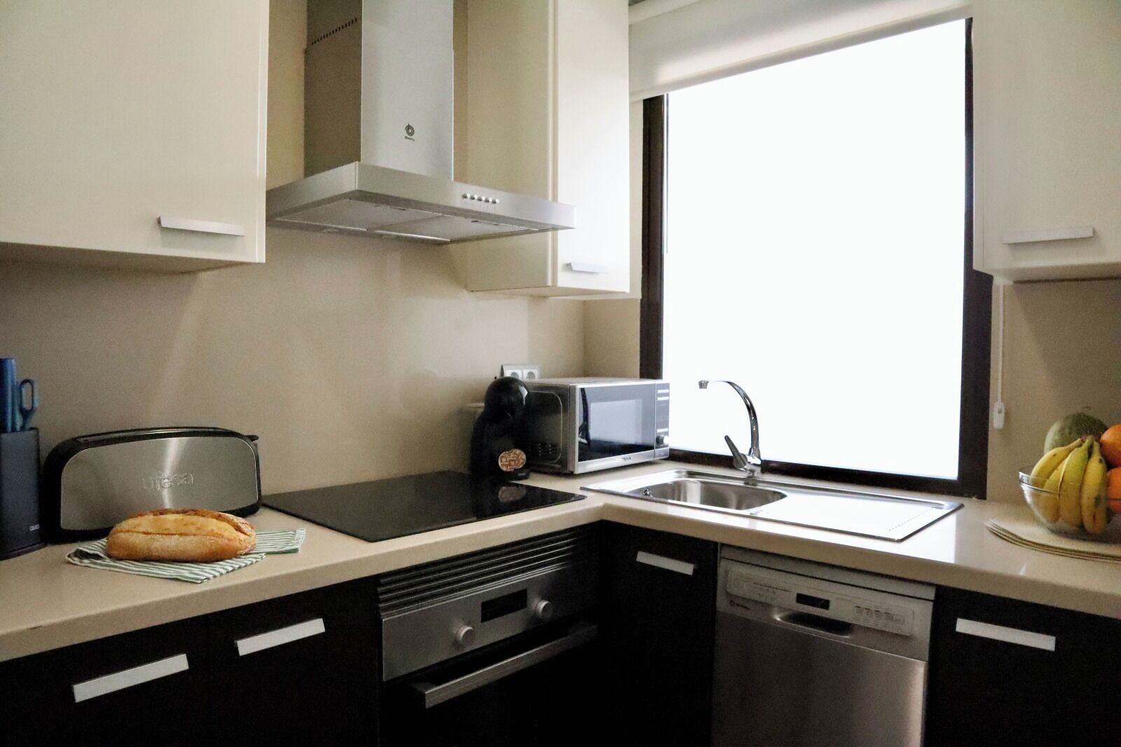 Una cucina moderna con microonde, tostapane e lavandino. C'è una finestra che permette l'illuminazione naturale e una ciotola di frutta sul bancone.