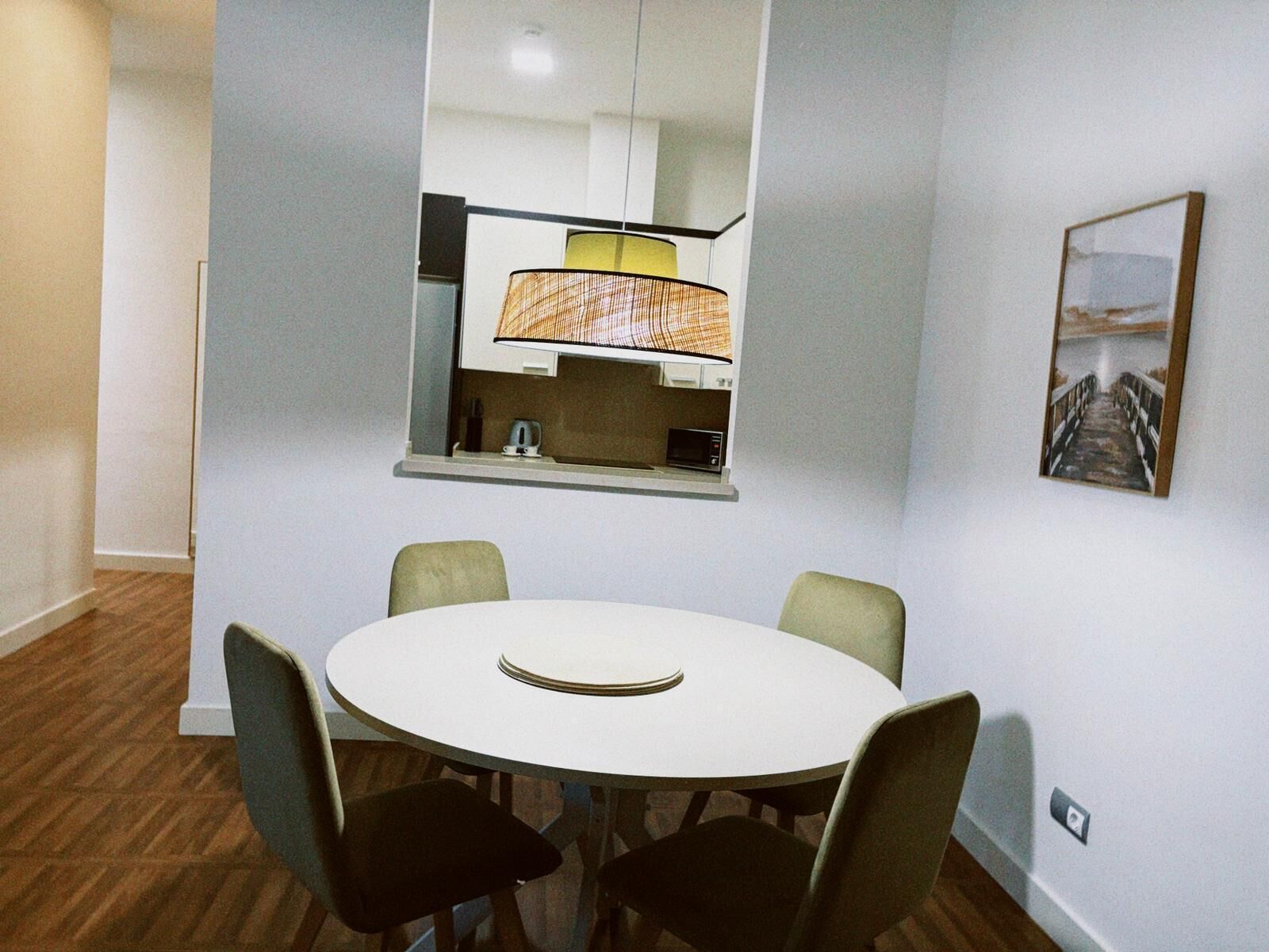 A compact dining area with a round table and four chairs, a kitchen with a microwave and a kettle, and a framed picture on the wall.