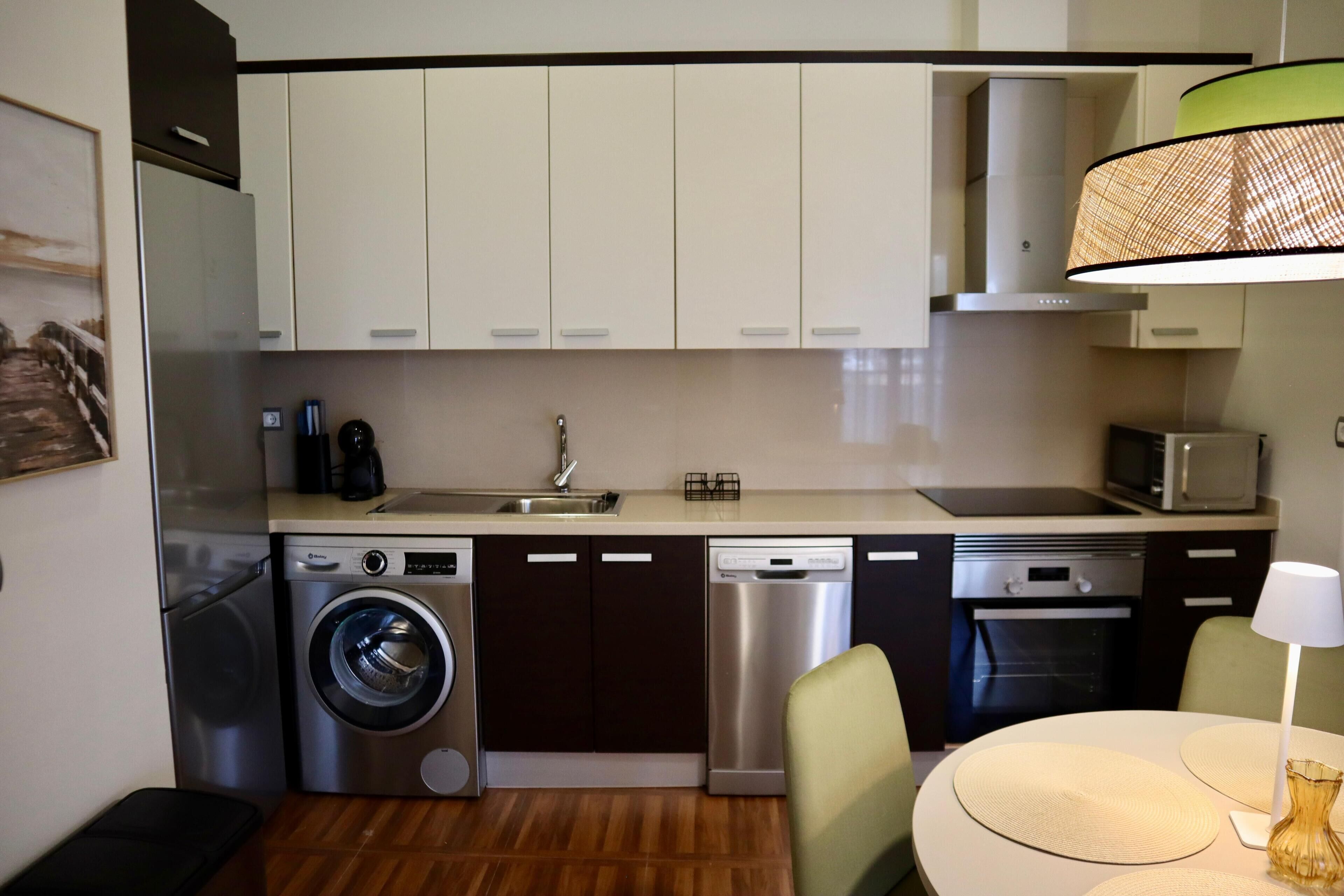 Cocina compacta equipada con lavadora, lavavajillas y microondas, y comedor con mesa y sillas.
