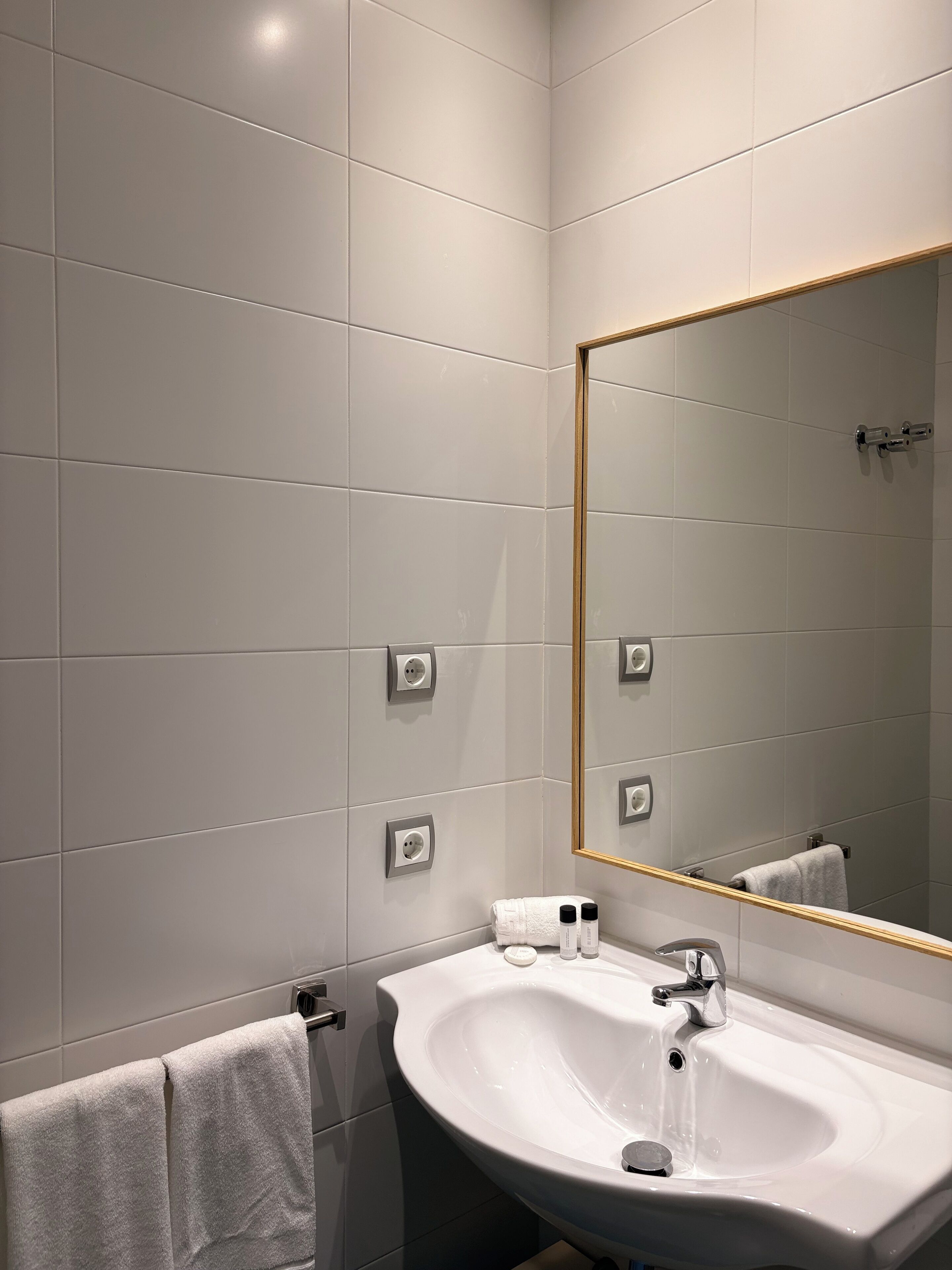 A modern bathroom with a white sink, a large mirror, and a towel rack.