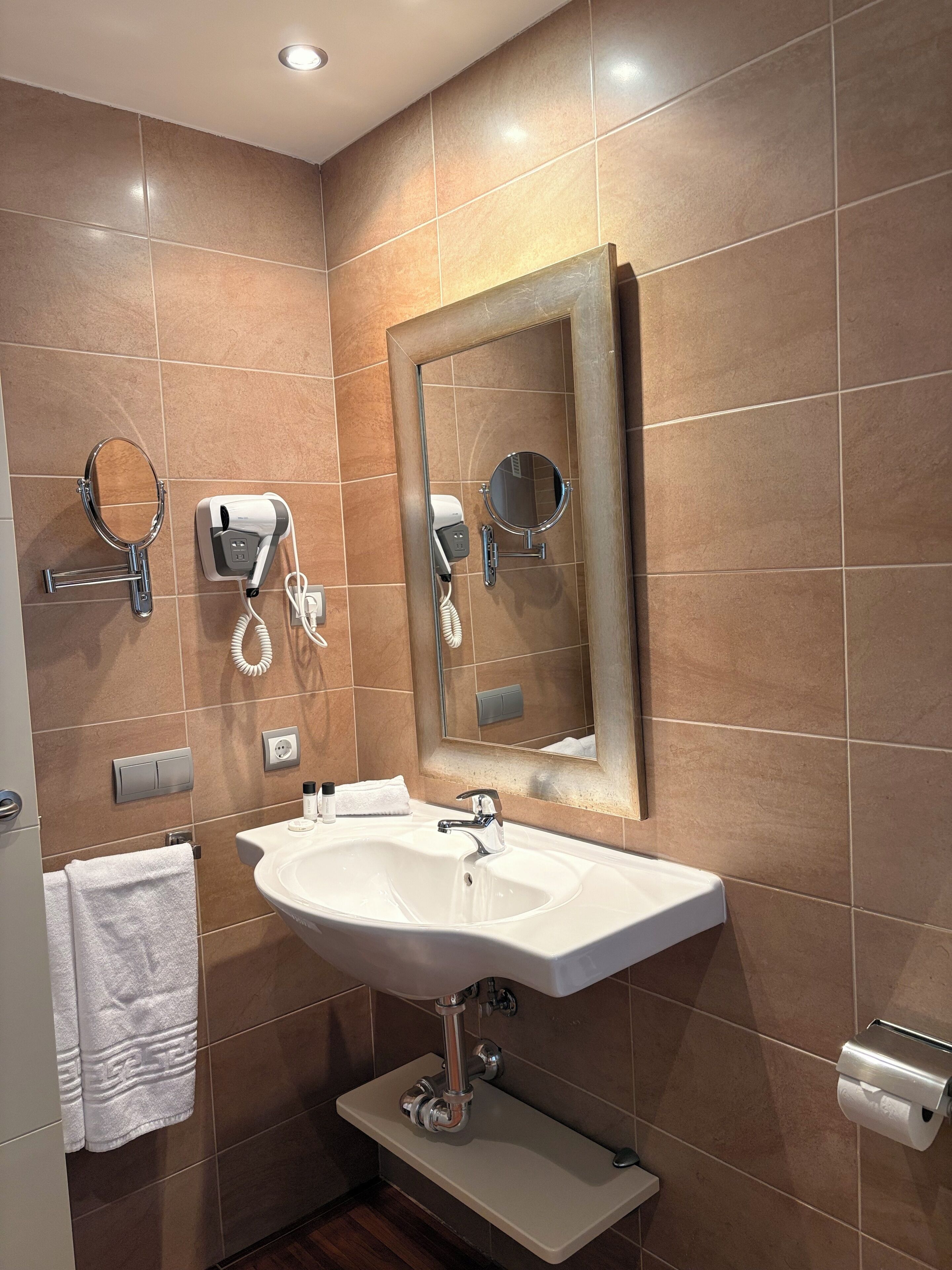 A modern bathroom with a large mirror, a sink, and a hairdryer on the wall.