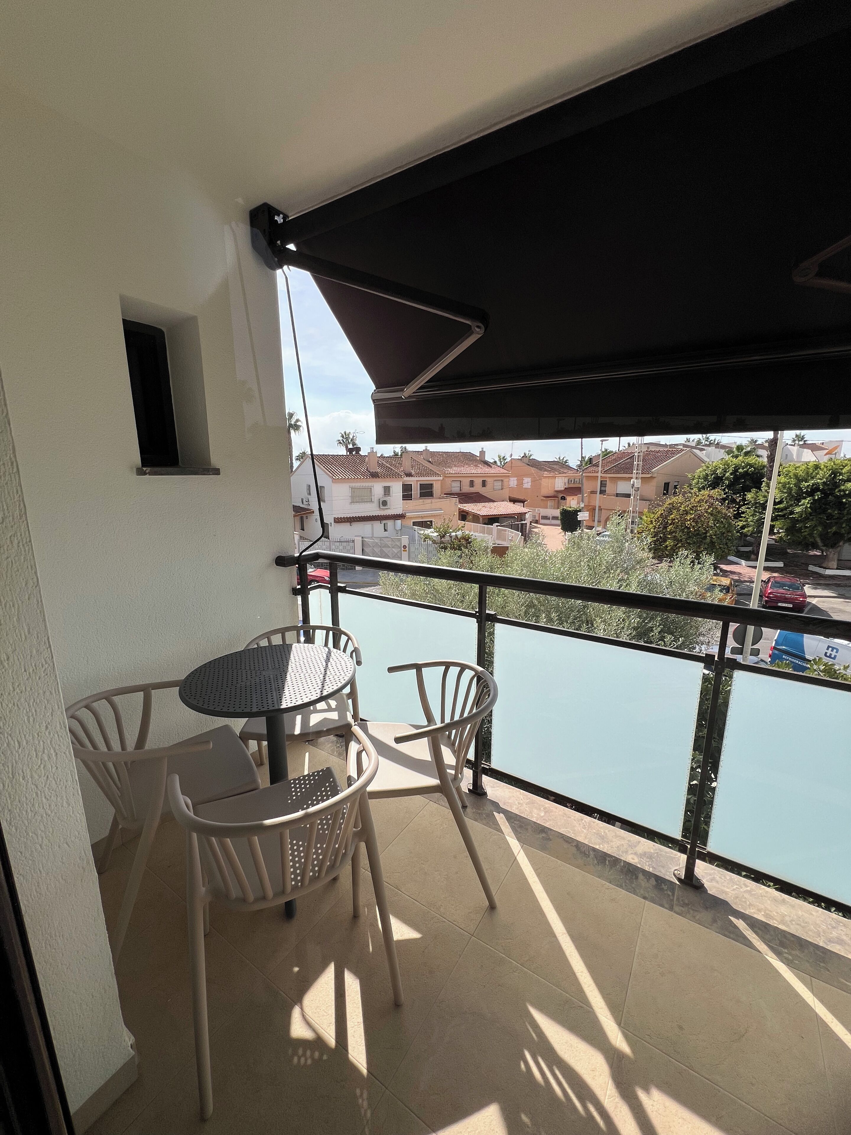 Un balcón con mesa y sillas, vista a un cuerpo de agua y edificios al fondo.