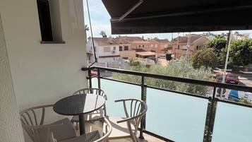 Un balcón con mesa y sillas, vista a un cuerpo de agua y edificios al fondo.