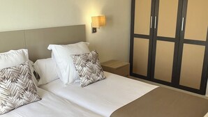 Et hotelværelse med to senge, et natbord, en lampe og et klædeskab.