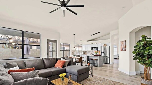 A modern living room with a grey sectional sofa, a wooden coffee table with yellow flowers, and a large window with a view of the kitchen. - Pool, Fun & Relaxation | Stylish Scottsdale Stay (Scottsdale)