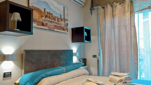 A hotel room with a bed, a nightstand, a lamp, a painting, and a window with curtains. - Luxury Herculaneum in Naples station train (Napoli)