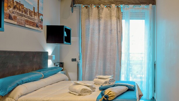 A hotel room with a bed, a television, a window with curtains, and a painting on the wall. - Luxury Herculaneum in Naples station train (Napoli)