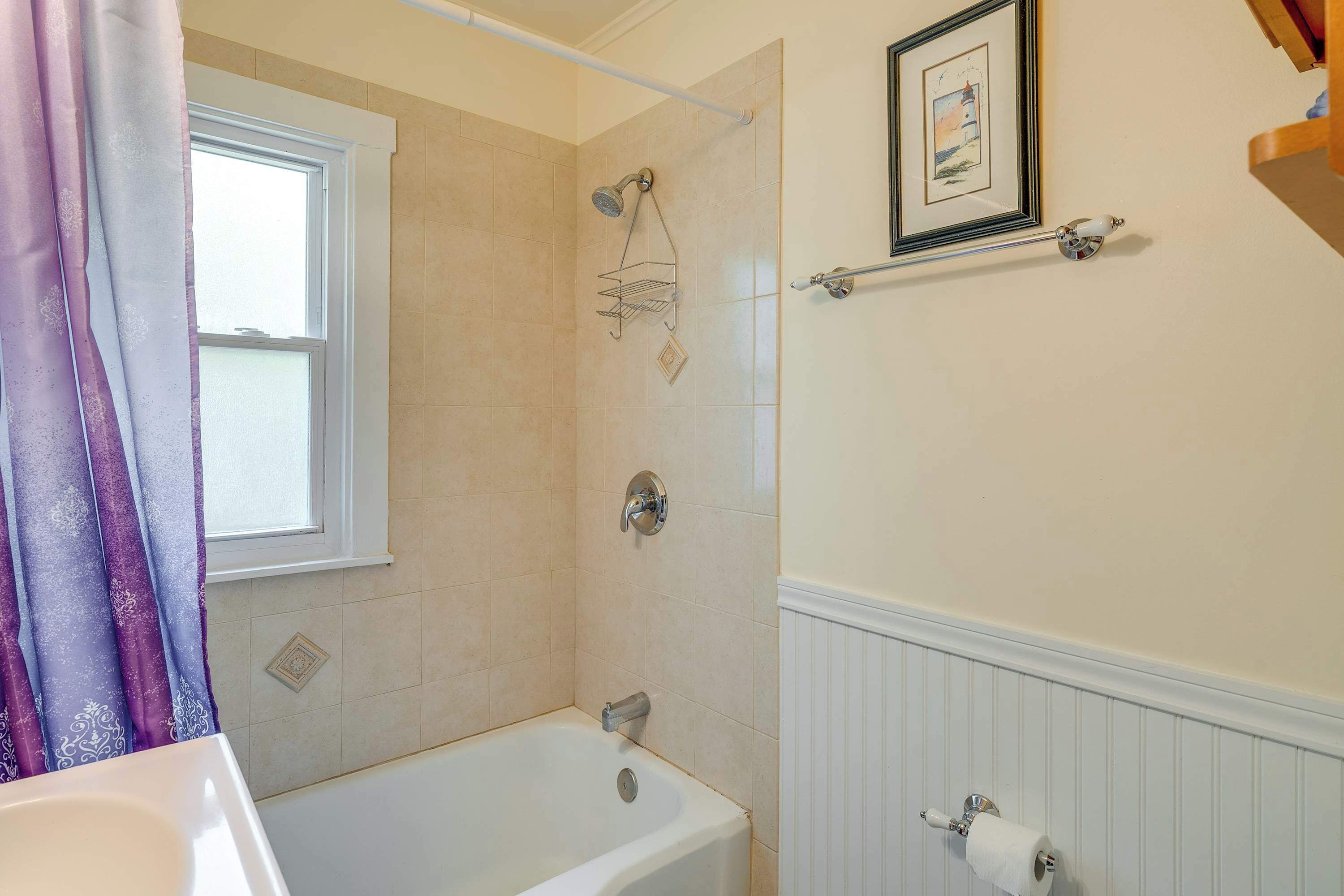 A bathroom with a bathtub, a shower, a window, and a toilet paper holder on the wall.
