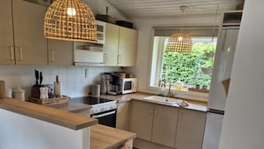 Una cocina moderna con suelo de madera, armarios blancos, una isla central e iluminación colgante.
