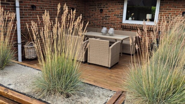 Un patio con un banco de madera, muebles de mimbre y hierbas altas.