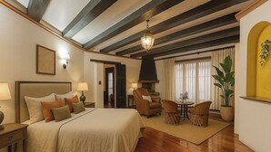 Une chambre d’hôtel dotée d’un grand lit, d’un coin salon avec des fauteuils, d’une cheminée et offrant une vue sur l’extérieur.