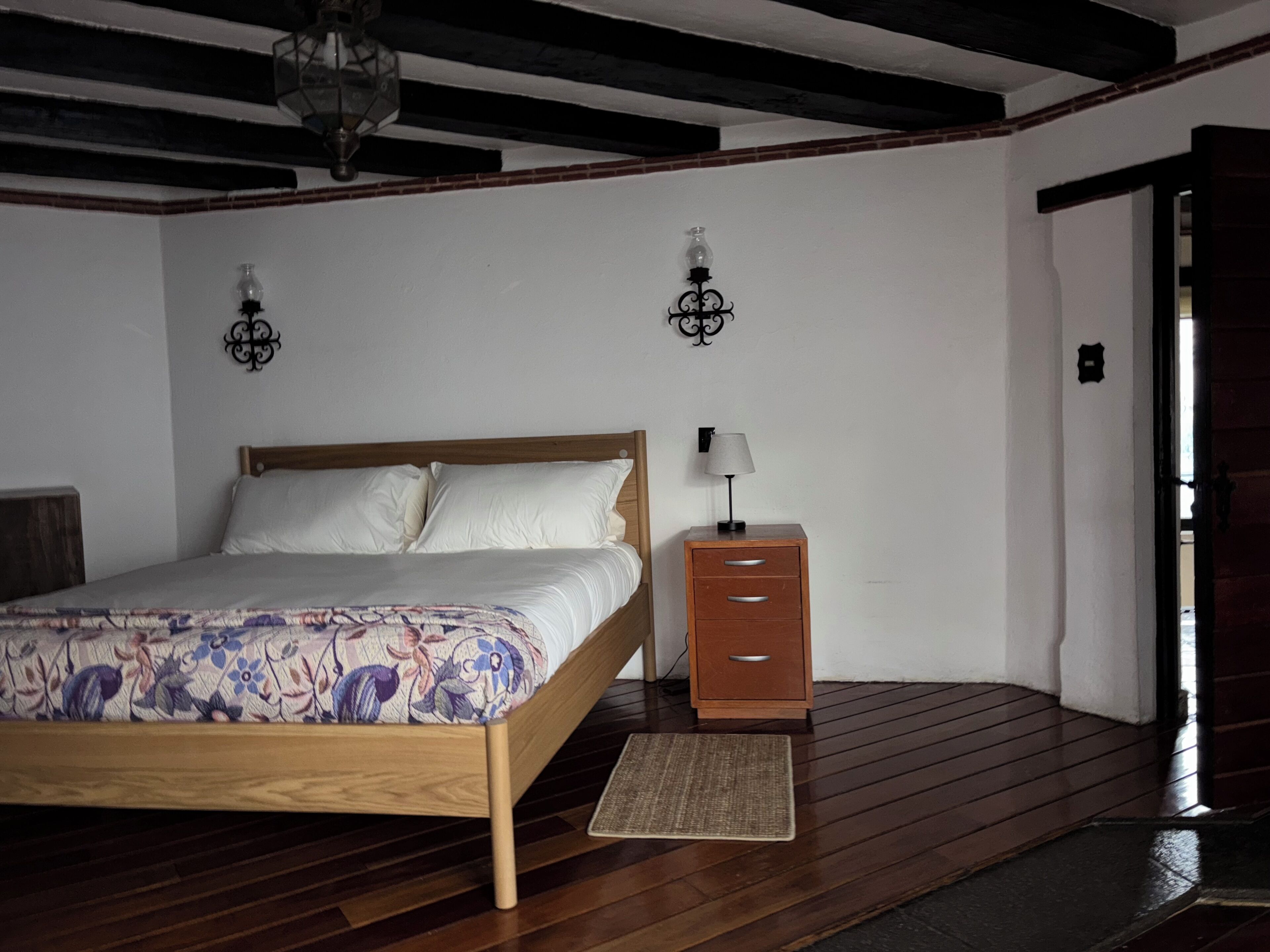 Een slaapkamer met een houten bed, een nachtkastje met een lamp en een klein vloerkleed.