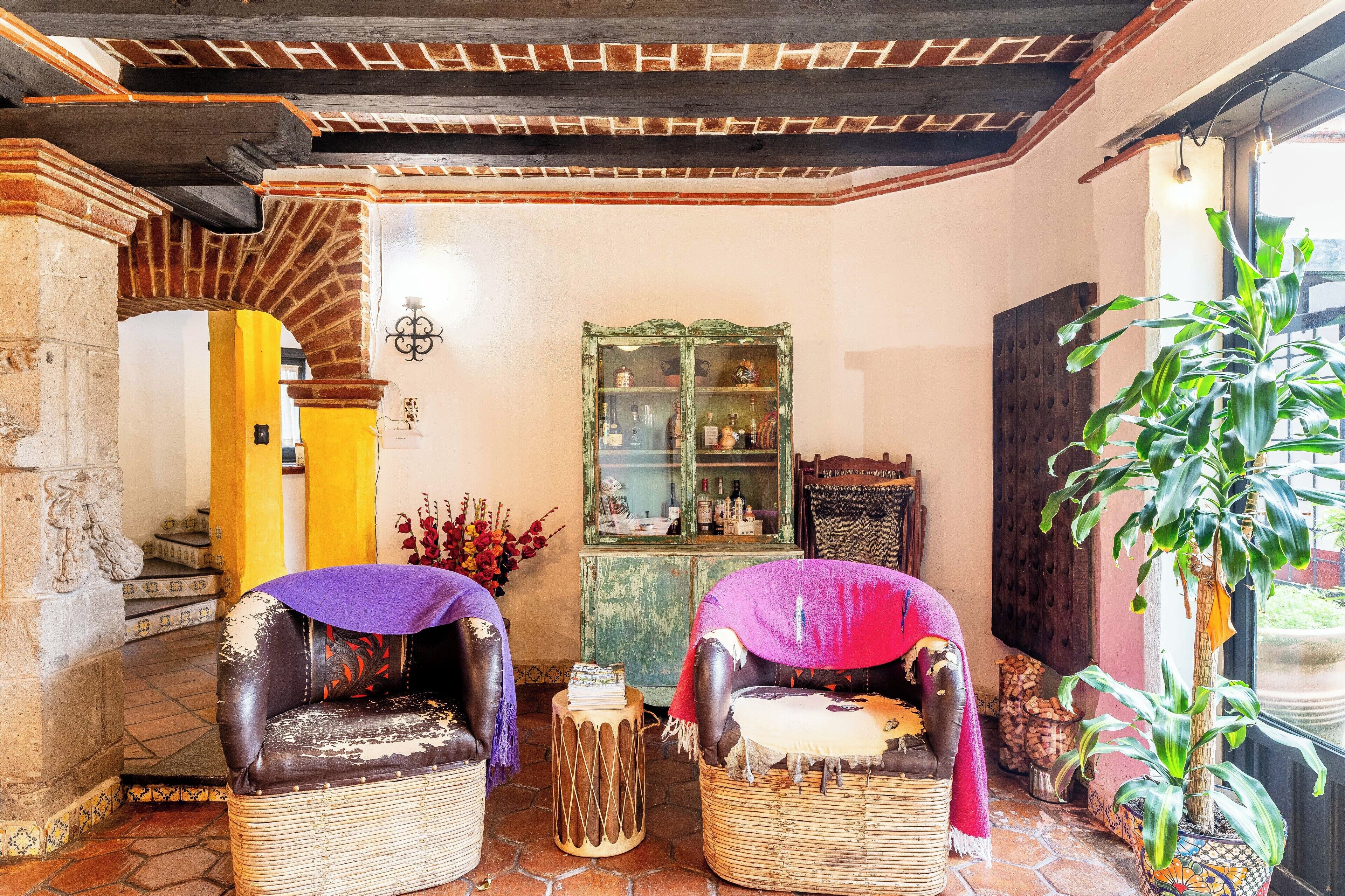 A cozy room with two wicker chairs, a wooden cabinet with glass doors, a potted plant, and a stone wall.