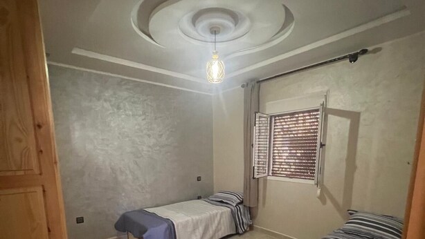 Ein Schlafzimmer mit zwei Betten, einem Fenster mit Jalousien, einer Deckenleuchte und einer Holztür.