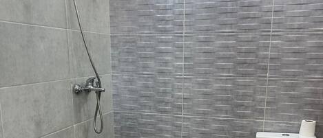 Une salle de bain avec une douche, des toilettes et un seau posé sur le sol.