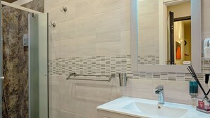 A bathroom with a glass shower enclosure, a sink with a mirror above it, and a towel rack. - Luxury Paestum in Naples station train (Napoli)
