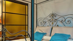 A bed with a metal frame and a blue bedspread, a window with yellow blinds, and a decorative wall panel. - Luxury Paestum in Naples station train (Napoli)