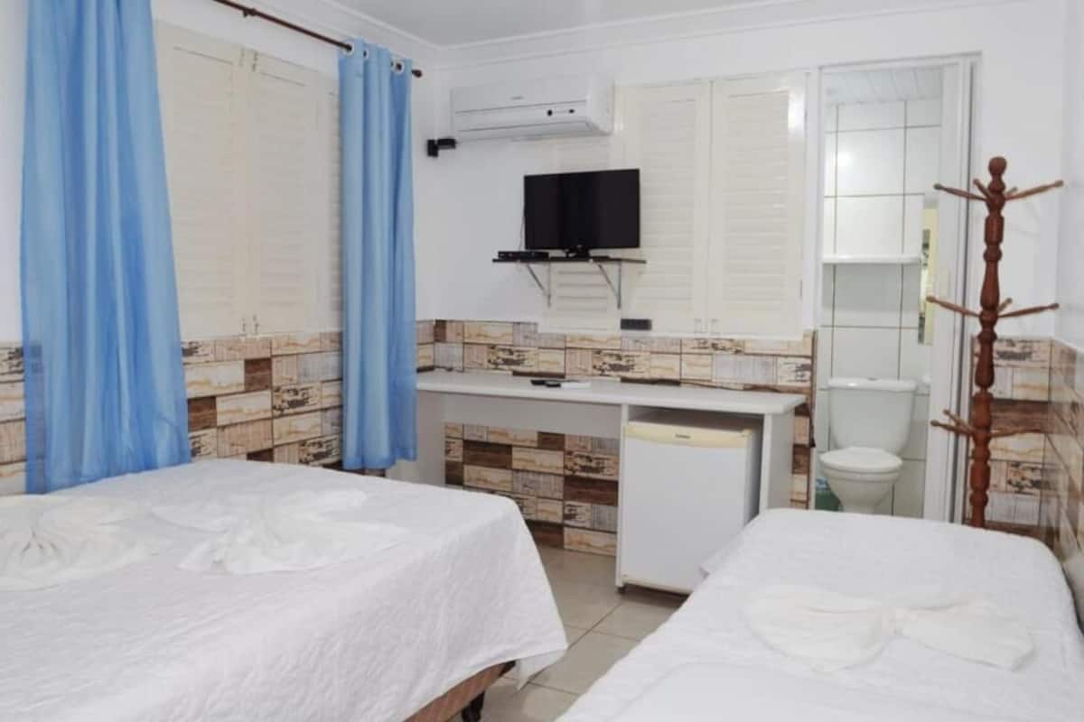 Une chambre d’hôtel avec deux lits, un petit bureau avec une télévision, une salle de bain avec des toilettes et un lavabo, et un espace douche.