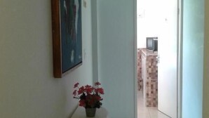 Een hal met een witte muur, een schilderij, een klein tafeltje met bloemen en een betegelde vloer die naar een keuken leidt.