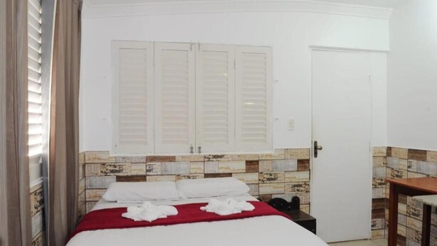Een hotelkamer met een bed, een kledingkast, een tafeltje en een betegelde muur.